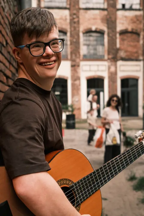 Uśmiechnięty chłopak z gitarą na podwórku starej kamienicy